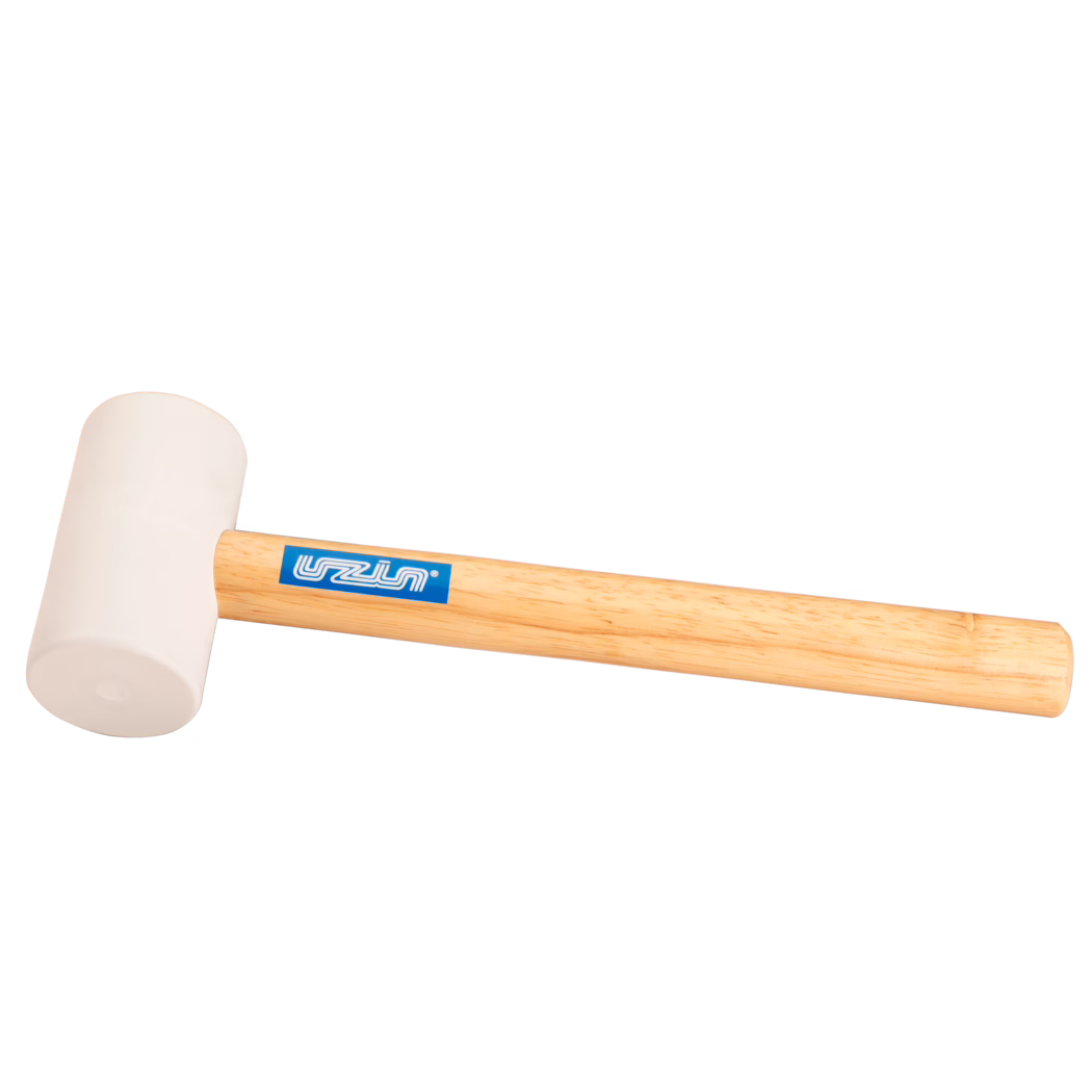 UZIN_Dummy_rubber hammer-UZIN_2014-11 Photo produit en gros plan d'un maillet en caoutchouc : tête en caoutchouc beige clair fixée à un manche en bois clair lisse avec un autocollant de marque rectangulaire bleu ; l'outil est posé en diagonale sur un fond blanc, éclairage doux mettant en valeur la texture du caoutchouc et le veinage du bois ; destiné aux frappes délicates en menuiserie, montage ou pose de carrelage.